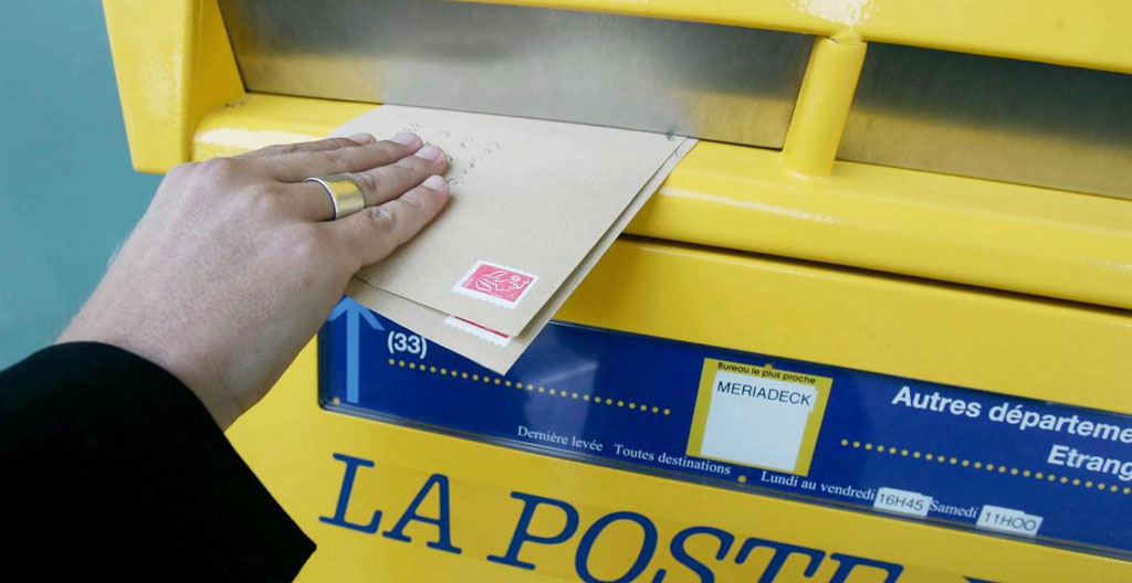 File d'attente dans un bureau de poste français avec plusieurs personnes attendant pour déposer leurs courriers recommandés papier
